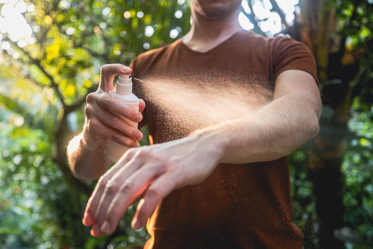 Person spraying insect repellent on forearm.