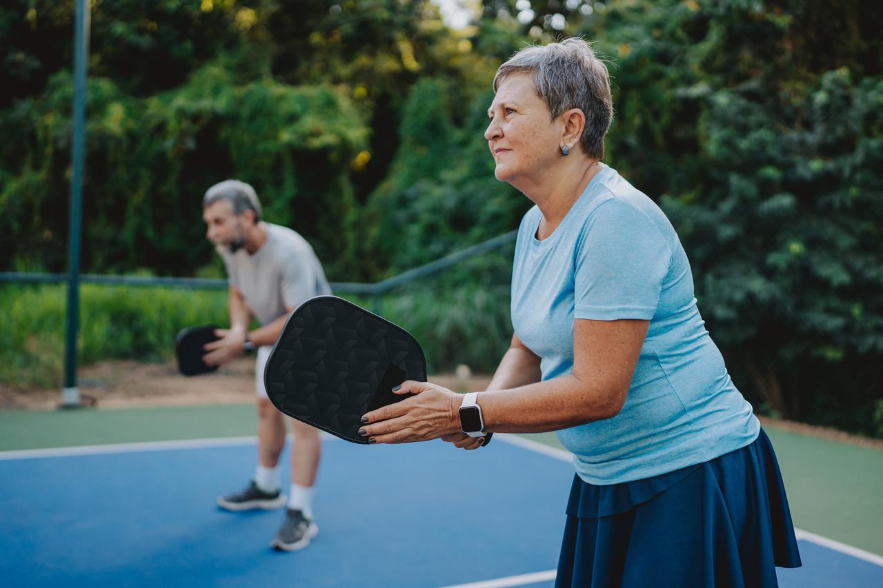 Older woman focused while playing pickleball outdoors.