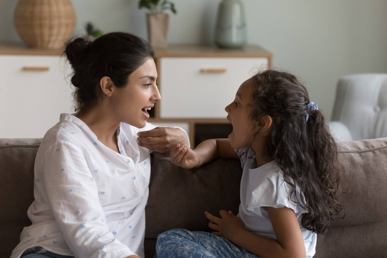 Mother and daughter practicing speech therapy together at home on a couch