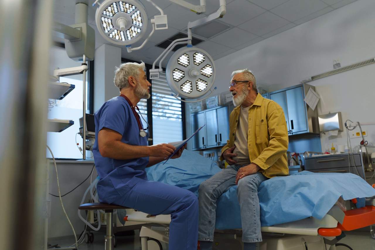 Older gentleman sitting on hospital bed and talking with a doctor
